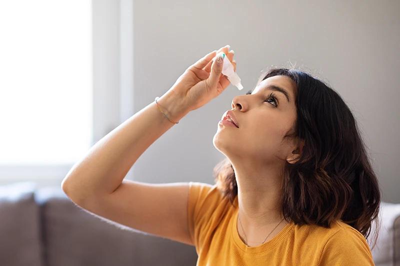a young woman putting in eye drops at home